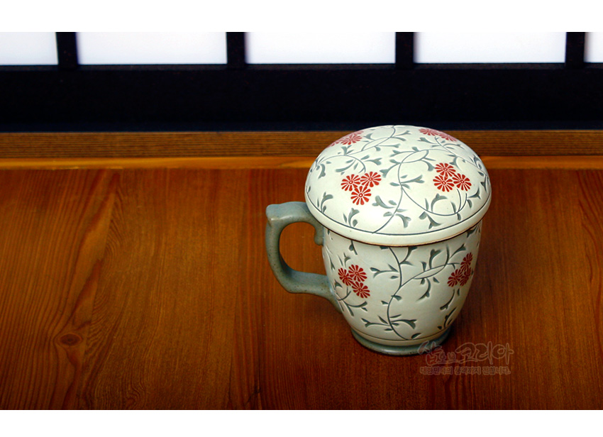 [텍스트: 샵오브코리아 대한민국 전통문화 (관광기념) 전문] 백자 재질에 상감 기법으로 표현된 적색 국화꽃과 회청색 덩굴무늬가 둘러진 뚜껑 있는 머그형 다기잔 모습