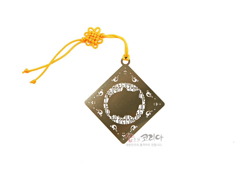 [텍스트: 샵오브코리아 대한민국의 품격까지 전합니다.] 금속 재질 사각 책갈피에 돼지 실루엣 투각과 백색 문양 장식, 노란 전통 매듭끈이 어우러진 디자인