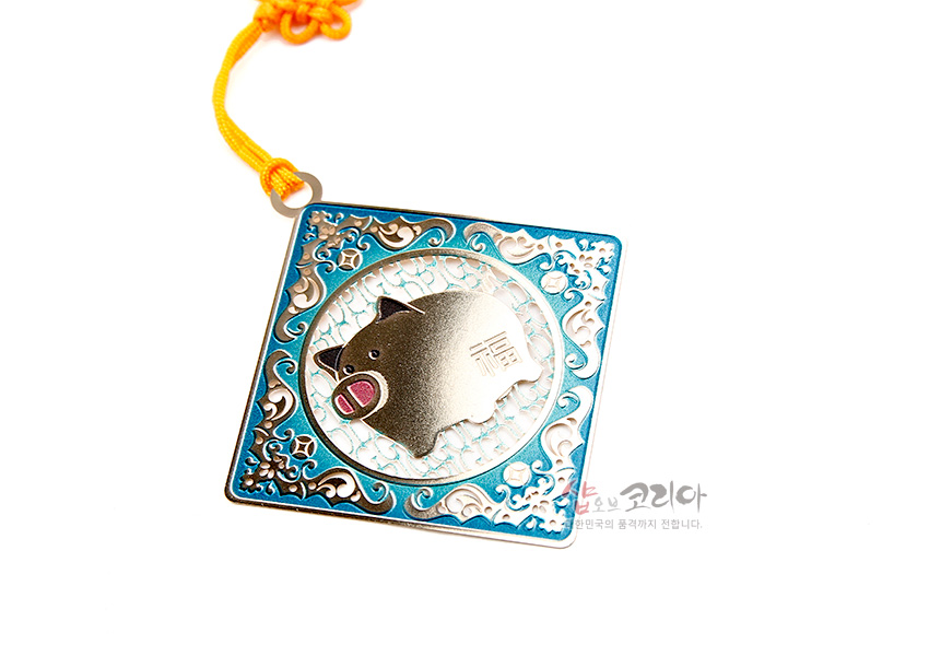 [텍스트: 福] 청록색 에나멜 장식 금속 정사각 틀 안에 돼지와 복자 문양이 새겨지고 노란 전통 매듭끈이 더해진 책갈피 장식