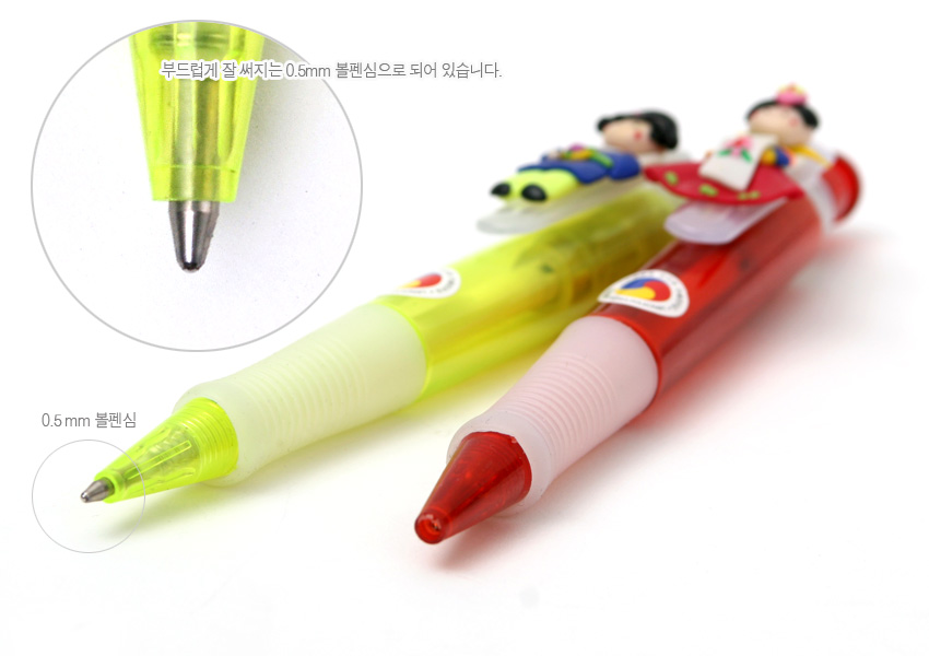 [텍스트: 부드럽게 잘 써지는 0.5mm 볼펜심으로 되어 있습니다. / 0.5mm 볼펜심] 반투명 형광 노랑·레드 플라스틱 바디와 태극 문양, 한복 입은 소형 인형 장식이 조화를 이루는 0.5mm 볼펜 디자인
