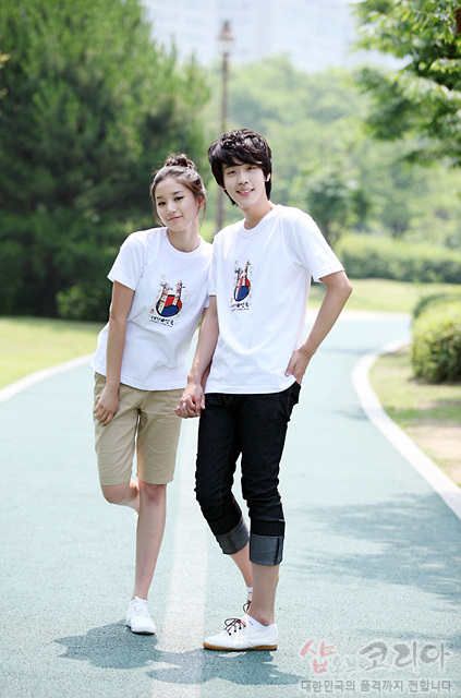 [텍스트: 샵코리아 대한민국의 품격까지 전합니다] 흰색 면 티셔츠에 장승 형상과 태극 문양을 색감 있게 배치한 3D 입체 전통 그래픽 디자인 이미지