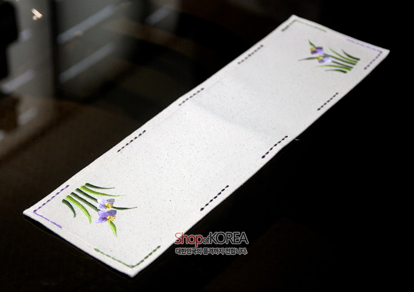 [텍스트: ShopofKOREA 대한민국의 품격까지 전합니다] 광목 재질의 긴 직사각 식탁보에 사군자 난초 문양과 잎을 연보라·초록색 자수로 수놓고 가장자리를 스티치로 마감한 전통 패브릭 장식