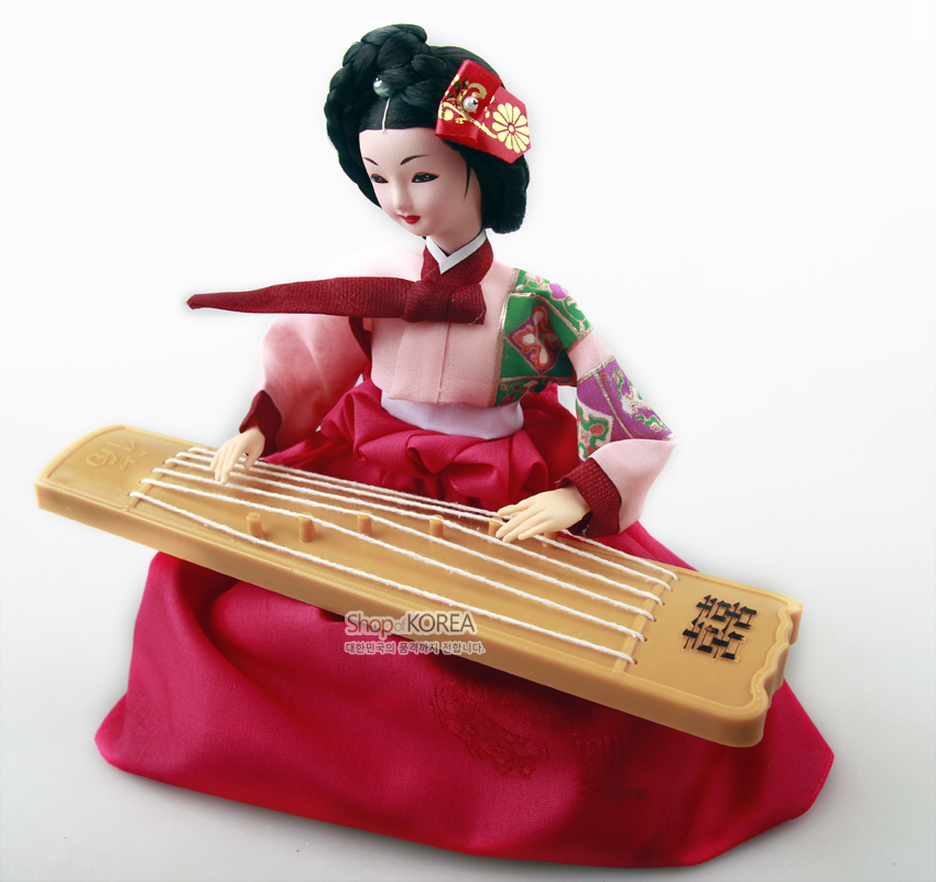 [텍스트: Shop KOREA 대한민국의 품격까지 전합니다.] 분홍색 비단 치마와 배색 저고리, 자수 머리장식, 나무 질감 가야금을 표현한 한복 인형 장식