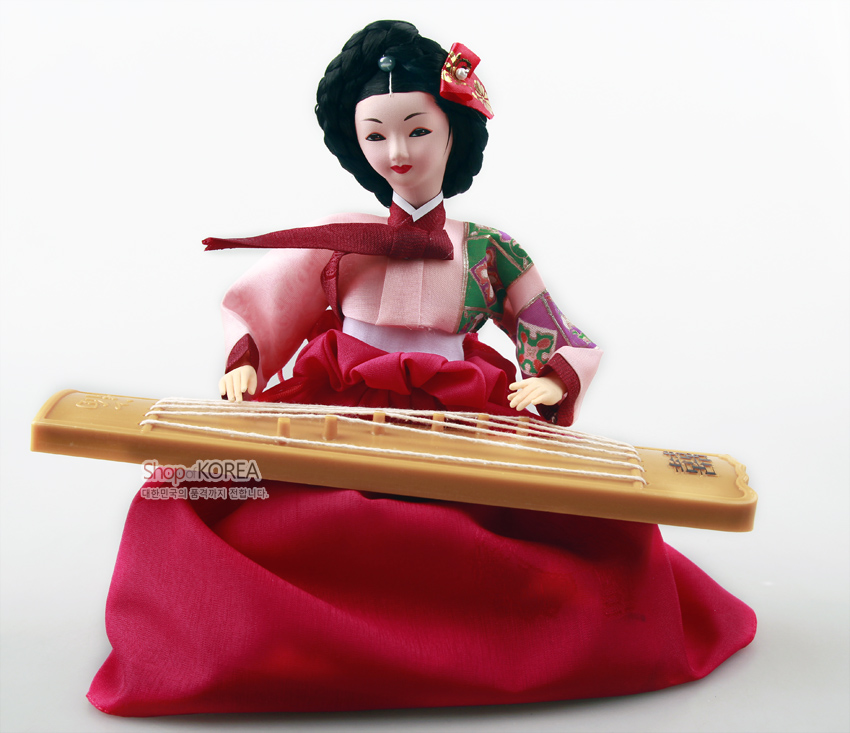 [텍스트: Shop of KOREA 대한민국의 품격까지 전합니다.] 분홍 비단 치마와 배색 패치워크 저고리, 장식 비녀 머리 장식, 나무 질감 가야금을 연주하는 전통 한복 인형 모습