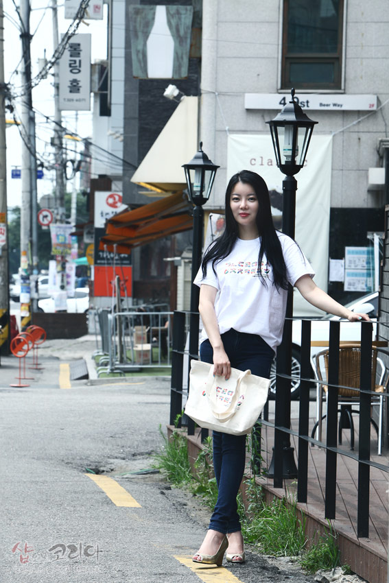 [텍스트: ㄱㄴㄷㄹㅁㅂㅅ ㅇㅈㅊㅋㅌㅍㅎ] 흰색 면 티셔츠와 에코백 중앙에 다채로운 색상의 한글 자음 가로 배열을 입체발포 기법으로 표현한 거리 연출 이미지