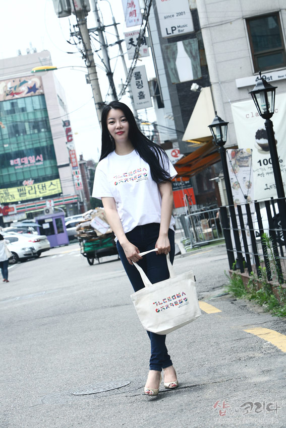 [텍스트: ㄱㄴㄷㄹㅁㅂㅅ ㅈㅊㅋㅌㅍㅎ] 흰색 면 티셔츠와 에코백에 다채로운 색상의 한글 자음 가로 배열 입체발포 프린트가 적용된 캐주얼한 거리 연출 이미지