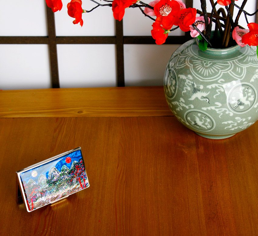 자개 상감 기법으로 일월오봉도 산수와 해·달, 소나무를 표현한 금속 테두리 명함집과 청자 학문 양각 무늬 화병의 조화로운 연출 이미지