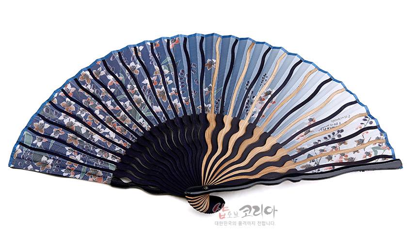 [텍스트: 샵오브코리아 대한민국의 품격까지 전합니다.] 남색에서 하늘색으로 이어지는 그라데이션 실크천에 물결형 대나무살이 배치되고, 잎과 도라지꽃 문양이 섬세하게 인쇄된 전통 접이식 부채 모습
