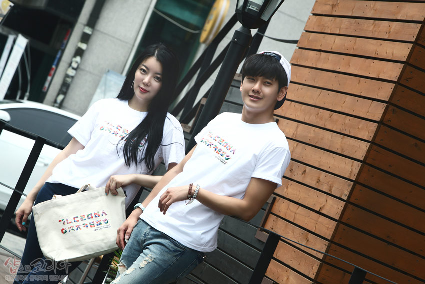 [텍스트: 샵오브코리아] 흰색 면 티셔츠와 에코백 위에 다채로운 색상의 한글 자음이 가로 배열로 입체발포 인쇄된 캐주얼 거리 패션 연출 모습