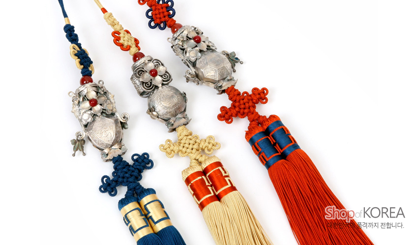 [텍스트: Shop of KOREA, 정교한 작품의 품격까지 전합니다.] 은제 호랑이와 장미 장식, 붉은 구슬 장식이 결합된 삼작투호에 청·황·홍 색 술과 전통 매듭 기법이 조화를 이룬 한복 노리개 세트 구성
