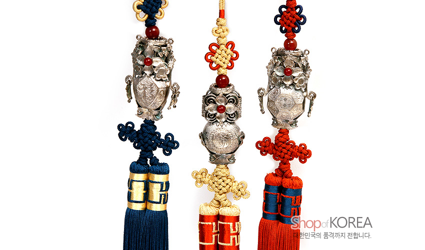 [텍스트: ShopofKOREA 대한민국의 품격까지 전달합니다.] 은 호랑이와 전통 문양을 정교하게 새긴 금속 장식에 붉은 구슬과 청·황·홍색 매듭, 술 장식이 조화를 이룬 삼작투호 노리개 세트 모습