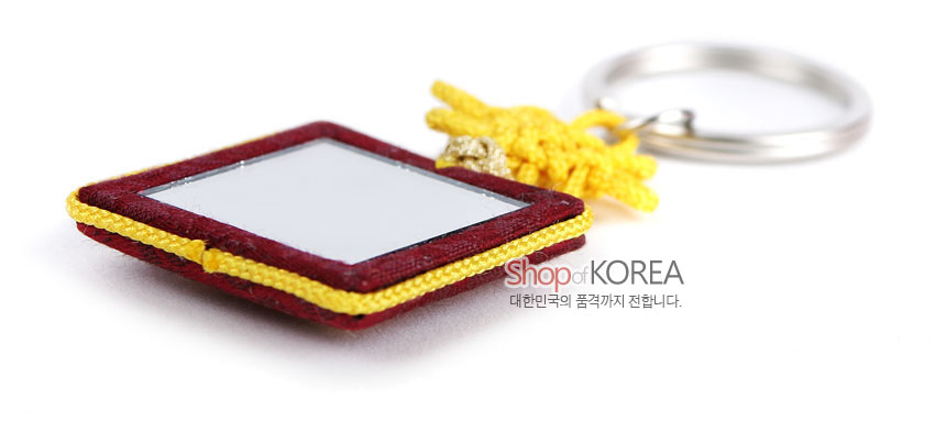 [텍스트: Shop of KOREA 대한민국의 품격까지 전합니다.] 자주색 비단 사각 거울 장식과 노란 전통 매듭, 금속 링 고리가 어우러진 열쇠고리 이미지 설명
