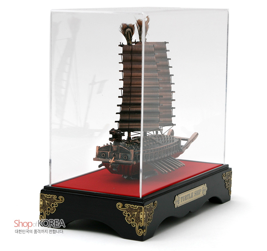 [텍스트: Shop of KOREA, TURTLE SHIP, 대한민국의 품격까지 전합니다.] 금속 질감의 동거북선 모형과 붉은 선체, 세밀한 노와 돛 표현, 금색 문양 장식의 흑색 받침대와 투명 아크릴 케이스 구성