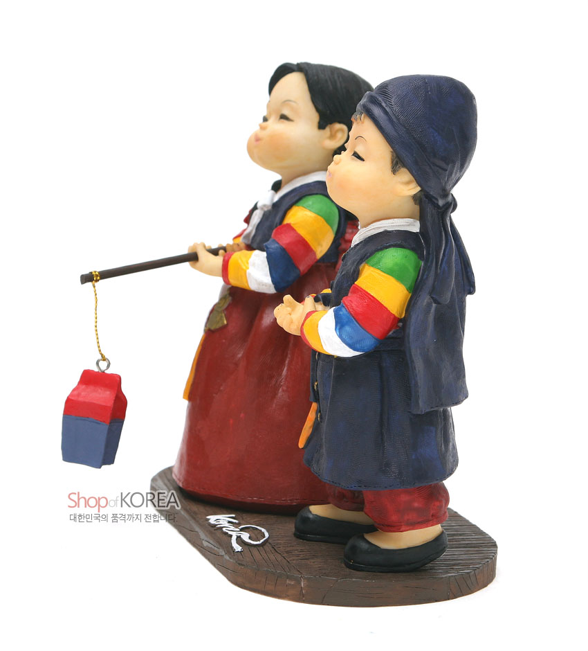 [텍스트: Shop of KOREA 대한민국의 품격까지 전합니다.] 색동 동정과 오방색 줄무늬 소매의 한복을 입은 소년·소녀 수지 인형, 청사초롱을 든 입체 조형 장식품