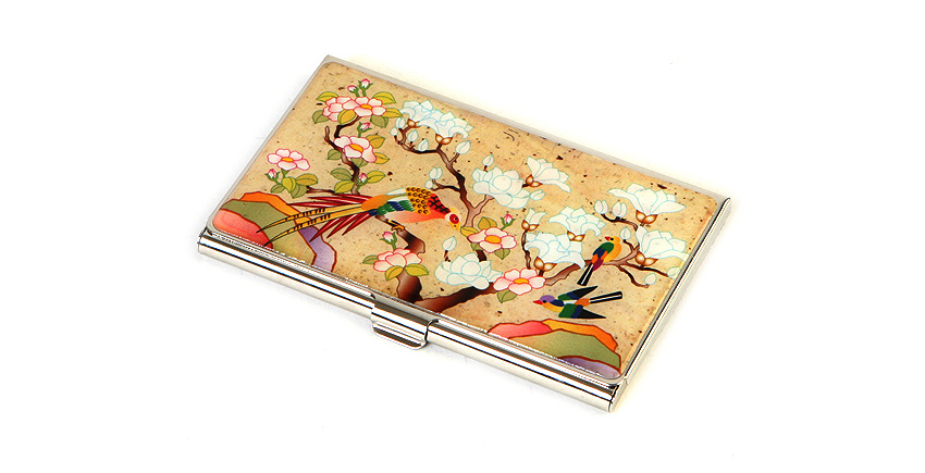 은은한 베이지 바탕 금속 명함케이스 위 자개 상감 기법으로 표현된 화조도, 흰 꽃과 화려한 새, 다채로운 색감의 조화로운 구성