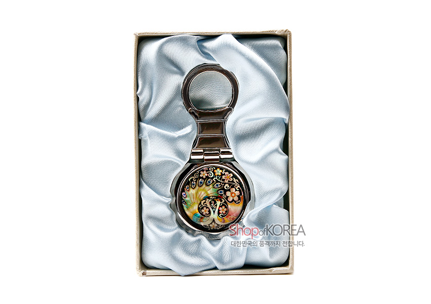 [텍스트: Shop of KOREA 대한민국의 품격까지 전합니다.] 금속 테두리에 자개 상감 기법으로 공작과 꽃문양을 넣은 다채로운 색감의 원형 열쇠고리 디자인 모습