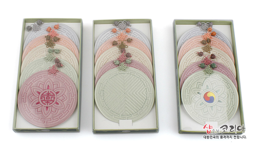 [텍스트: 샵오브코리아 대한민국의 품격까지 전합니다.] 전통 누비 기법의 원형 컵받침 세트, 연꽃·태극·기하학 문양과 파스텔 톤 색상, 조화로운 매듭 장식 구성