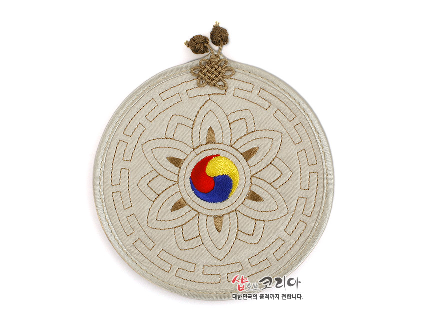 [텍스트: 샵오브코리아 대한민국의 품격까지 전합니다.] 전통 누비 기법으로 표현한 연꽃 문양과 중앙 삼색 태극 수놓음, 베이지색 원형 천 위 갈색 자수선과 윗부분 매듭 장식 컵받침 이미지 설명
