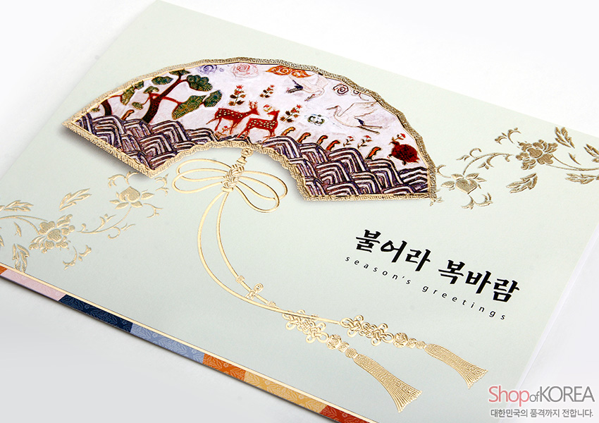 [텍스트: 불어라 복바람 / season's greetings] 부채 형 자개 상감에 산수와 사슴 문양을 더하고, 금박 매듭과 꽃문양, 파스텔 민트 배경이 어우러진 전통 연하장 디자인