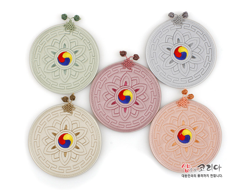 [텍스트: 샵오브코리아 대한민국의 품격까지 전합니다.] 전통 누비 기법의 원형 컵받침 5종, 파스텔톤 천 위에 연꽃·기하학 문양과 삼색 태극 자수, 상단 매듭 장식 특징
