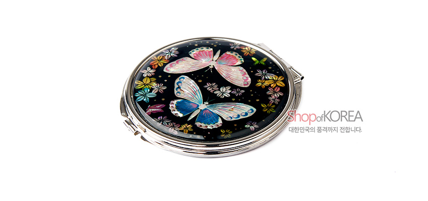 [텍스트: Shop of KOREA 대한민국의 품격까지 전합니다.] 검은 바탕 위 자개 상감 기법으로 표현된 나비와 꽃 문양이 돋보이는 원형 금속 손거울 디자인