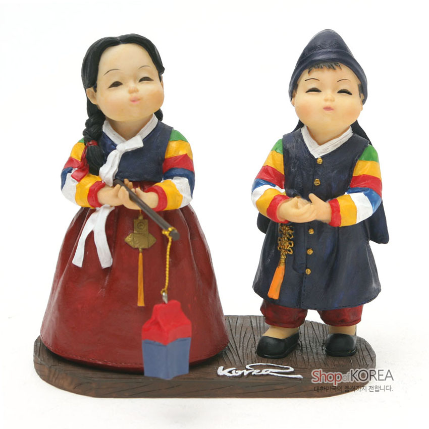 [텍스트: Shop of KOREA] 채색 수지 재질의 한복 차림 소년·소녀 인형, 색동 소매와 오방색 청사초롱, 나무 질감 받침대와 전통 매듭 장식 표현
