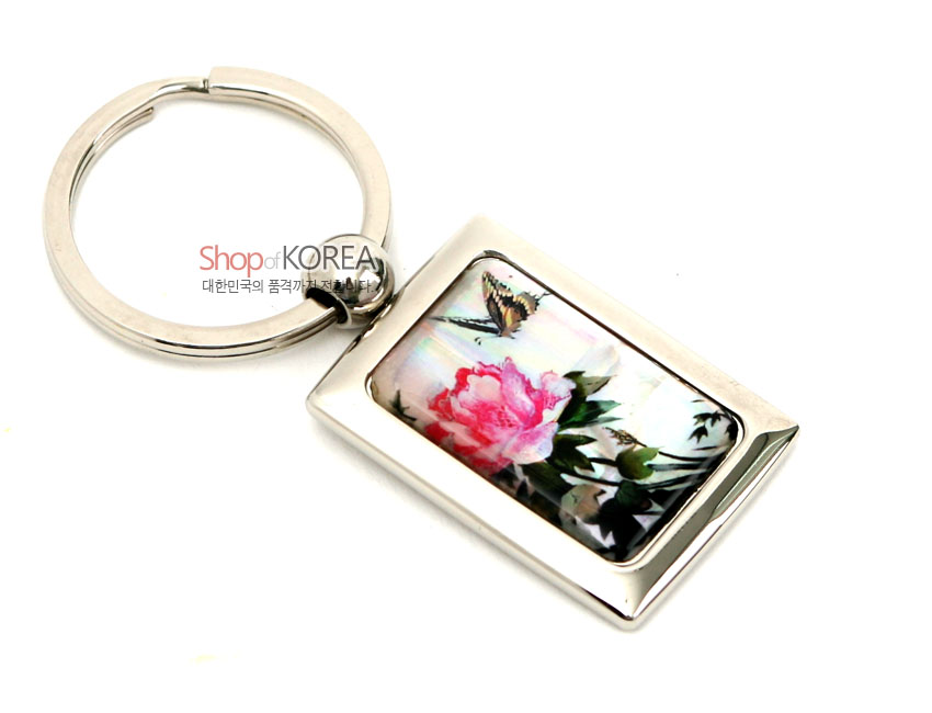 [텍스트: Shop of KOREA 대한민국의 품격까지 전합니다] 금속 사각 프레임 속 자개 판에 담홍색 꽃과 나비 문양을 채색 상감한 열쇠고리 디자인