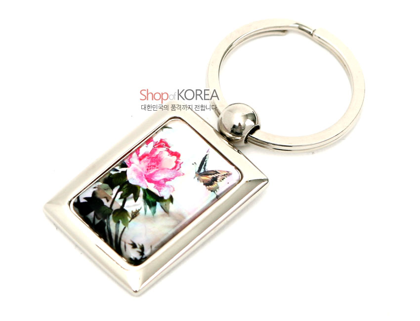 [텍스트: Shop of KOREA 대한민국의 품격까지 전합니다] 금속 사각 프레임에 채색 자개를 상감하여 담홍색 꽃과 나비 문양을 섬세하게 표현한 열쇠고리 디자인