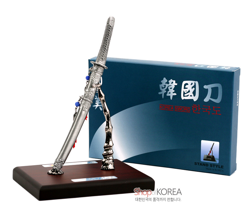 [텍스트: 韓國刀 KOREA SWORD 한국도 STAND STYLE Made in KOREA Shop of KOREA 대한민국의 품격까지 전합니다.] 금속 재질 한국도 모형과 대나무 형상 스탠드, 붉은 실 매듭과 청색 구슬 장식, 나무 받침대 구성이 특징인 장식품