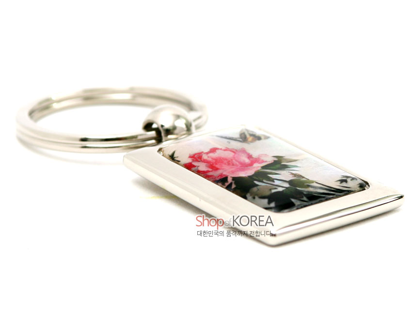 [텍스트: Shop of KOREA 대한민국의 품격까지 전합니다.] 금속 사각 프레임에 채색 자개를 상감하여 담홍색 꽃과 나비 문양을 넣은 열쇠고리 디자인