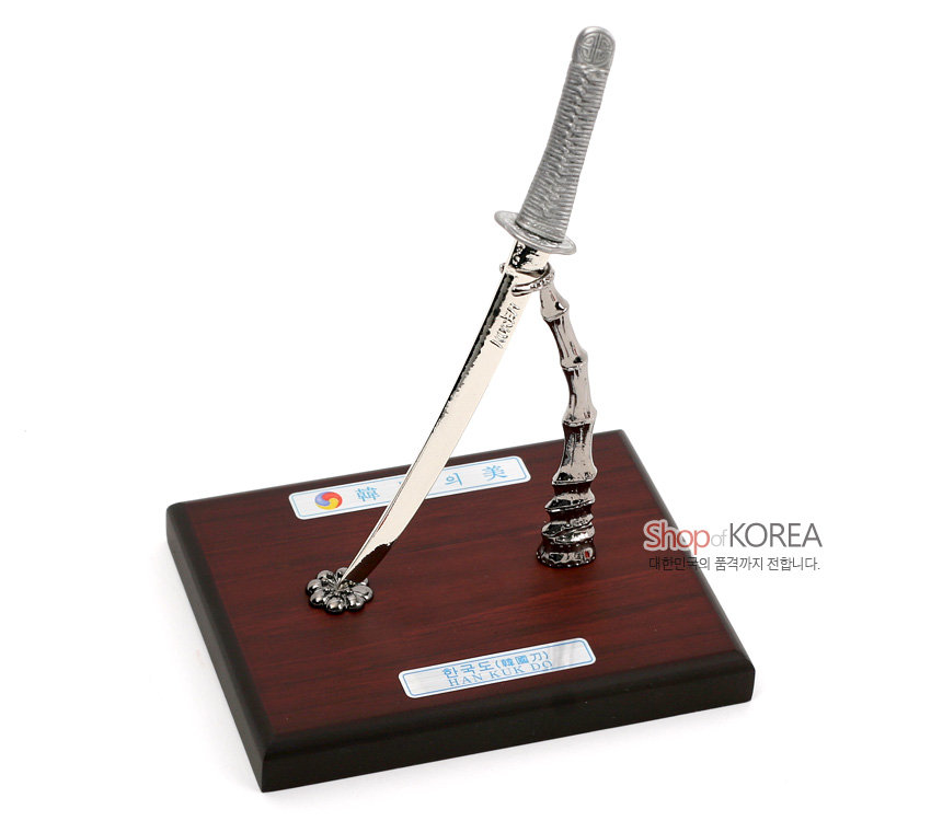 [텍스트: 韓의美 / 한국도(韓國刀) HANKUK DO / Shop of KOREA 대한민국의 품격까지 전합니다.] 금속 재질 한국도 모형과 대나무 형상 스탠드, 짙은 목제 받침대가 조화된 장식품