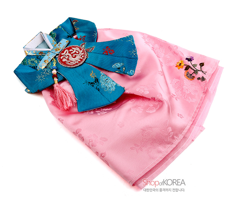 [텍스트: ShopofKOREA 대한민국의 품격까지 전합니다.] 청록색 비단 당의와 연분홍 비단 치마로 구성된 한복 형태 와인 커버, 금박 꽃문양 직조와 수놓은 국화 자수, 매듭술 장식이 조화를 이룬 디자인