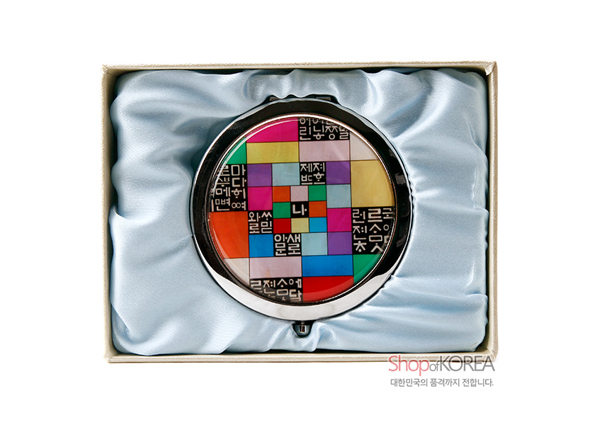 [텍스트: Shop of KOREA 대한민국의 품격까지 전합니다.] 금속 원형 테두리에 천연 자개 상감, 다채로운 조각보 색상과 흑백 훈민정음 문자 패턴이 어우러진 원터치 손거울 이미지 설명