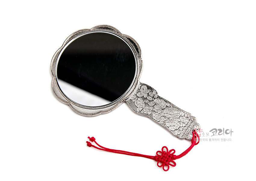 [텍스트: 샵오브코리아] 금속 재질에 섬세한 꽃과 나비 문양이 양각된 손잡이거울, 붉은 전통 매듭 장식이 더해진 디자인형 손거울