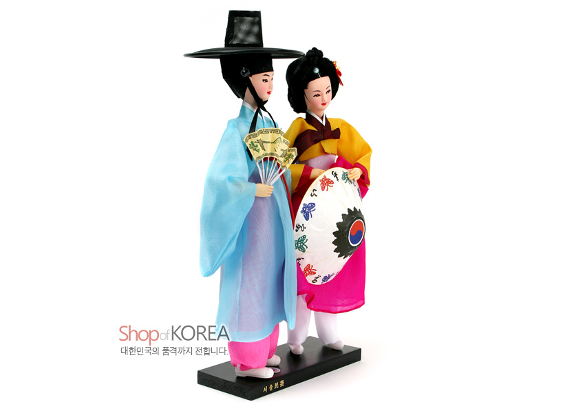 [텍스트: Shop of KOREA / 대한민국의 품격까지 전합니다 / 선비와어우동] 비단 느낌의 하늘색 도포와 색동 저고리, 태극 문양 부채와 나비 자수 장식이 돋보이는 한복 커플 인형 세트 모습