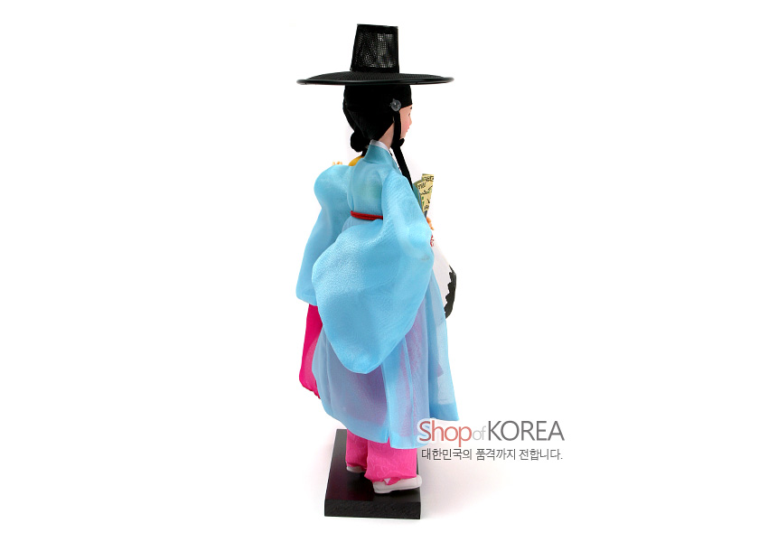 [텍스트: Shop of KOREA 대한민국의 품격까지 전합니다.] 옅은 하늘색 비단 저고리와 분홍 치마, 흑색 갓과 장식 머리카락이 조화를 이루는 한복 인형 측면 모습