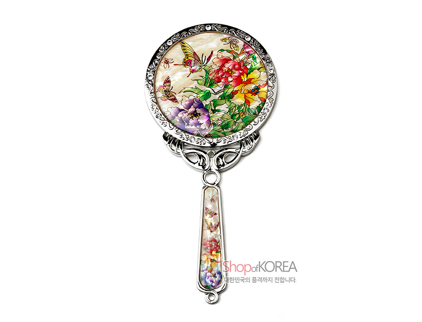 [텍스트: ShopofKOREA 대한민국의 품격까지 전합니다.] 자개 상감 옻칠 바탕에 목단꽃과 나비 문양을 화사한 색감으로 담고, 금속 손잡이에 자개 장식을 더한 원형 손거울 디자인