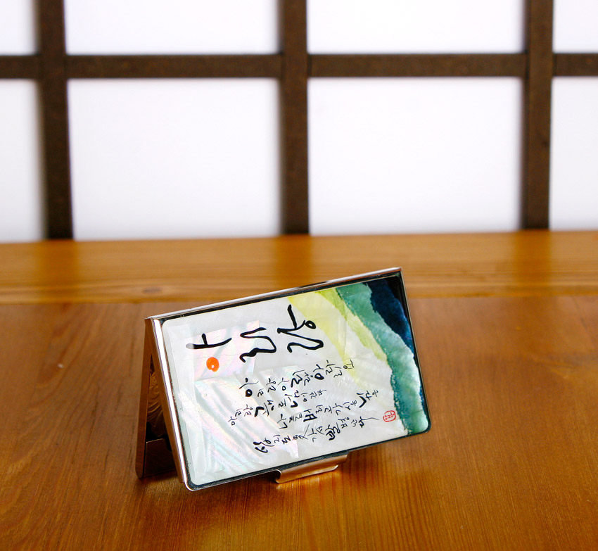 [텍스트: 아리랑 가사 서예] 금속 재질 위 진주빛 자개 바탕과 녹청색 수묵 그라데이션, 아리랑 가사 서예가 어우러진 직사각형 명함집 디자인