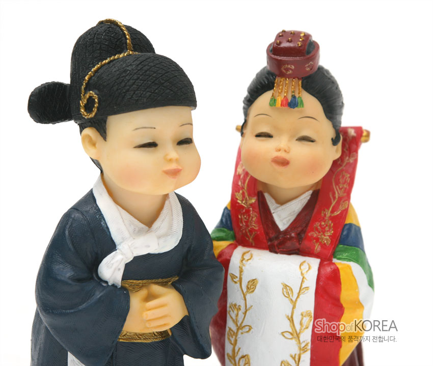 [텍스트: ShopofKOREA 대한민국의 품격까지 전합니다.] 레진 소재 전통혼례 신랑신부 인형, 남색 도포와 흰 동정, 오방색 색동과 금색 자수 문양 활옷 및 족두리 장식 표현