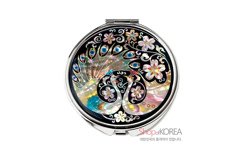 [텍스트: ShopofKOREA 대한민국의 품격까지 전합니다] 흑색 옻칠 바탕 위 자개 상감 기법으로 표현된 공작 한 쌍과 꽃문양, 오색 자개의 광택과 은색 금속 테두리의 조화가 돋보이는 원형 손거울 디자인