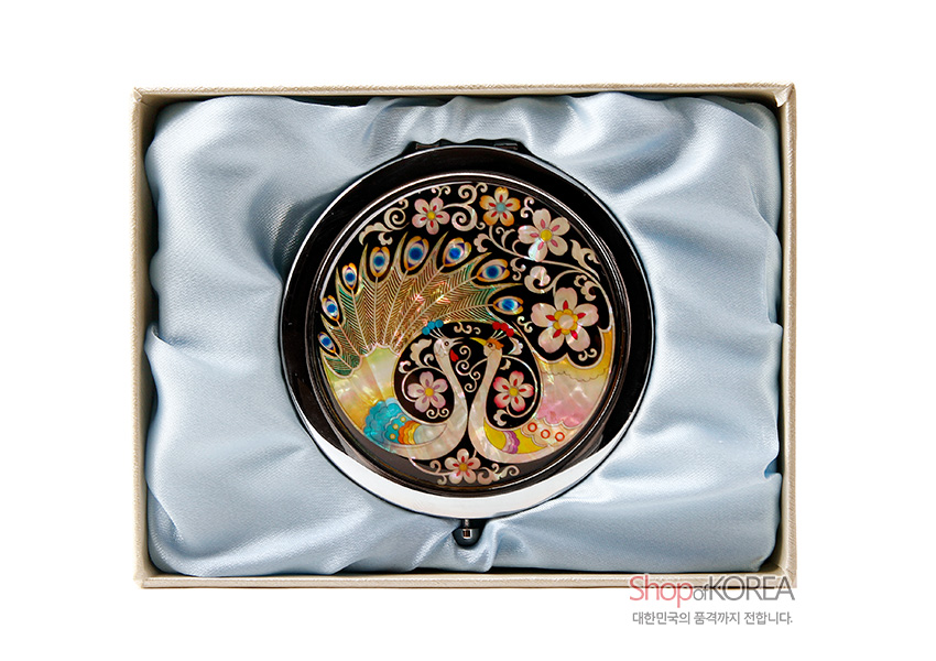 [텍스트: ShopKOREA 대한민국의 품격까지 전합니다.] 금속 테두리에 천연 자개 상감 기법으로 공작 한 쌍과 꽃문양을 다채로운 색감으로 표현한 원형 손거울