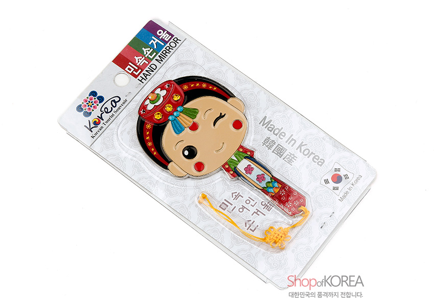 [텍스트: 민속손거울 HAND MIRROR Made In Korea 韓國産] 금속 재질 위 컬러 채색으로 표현된 한복 신부 캐릭터 손거울, 붉은색·초록색 한복과 꽃문양 족두리, 노란 매듭 끈 장식이 어우러진 디자인