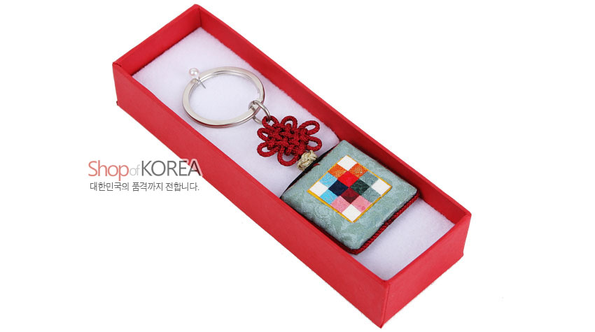 [텍스트: Shop of KOREA 대한민국의 품격까지 전합니다.] 옥색 비단 바탕에 다색 조각보 패턴이 놓인 방석형 장식과 붉은 전통 매듭, 금속 고리로 구성된 열쇠고리 디자인