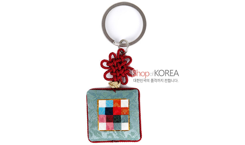 [텍스트: Shop of KOREA / 대한민국의 품격까지 전합니다.] 옥색 비단 바탕 방석형 패드에 다색 조각보 문양을 배치하고 붉은 전통 매듭과 금속 고리를 더한 열쇠고리 이미지 설명
