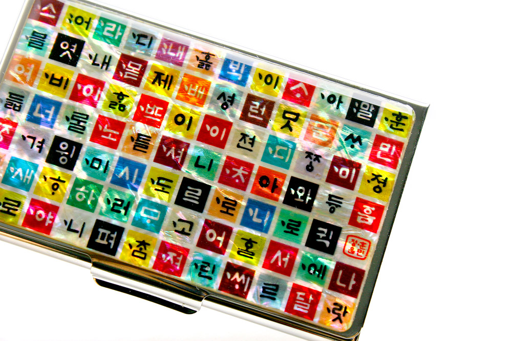 [텍스트: 훈민정음] 금속 테두리 위 자개 바탕에 형형색색 정사각 칸을 배열하고 훈민정음 자모를 넣어 모자이크처럼 구성한 명함집 디자인
