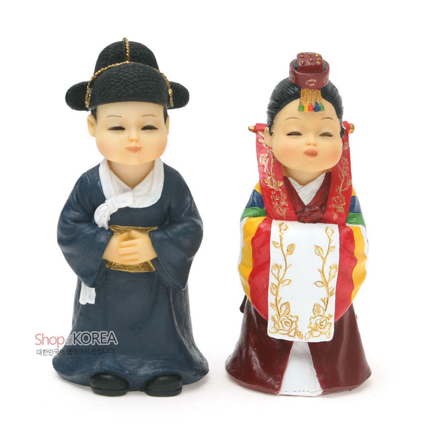[텍스트: Shop of KOREA 대한민국의 품격까지 전합니다.] 레진 소재 전통혼례 신랑신부 인형, 남색 도포와 흑립, 오방색 색동 소매와 금색 꽃문양 수보가 돋보이는 활옷 장식 조형물