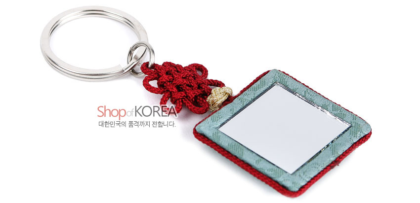 [텍스트: Shop of KOREA, 대한민국의 품격까지 전합니다.] 금속 링과 붉은 전통 매듭, 옥색 비단 테두리와 붉은 비단 바탕에 사각 거울이 삽입된 조각보 스타일 열쇠고리 이미지 설명