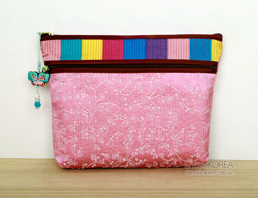[텍스트: Shop of KOREA 대한민국의 품격까지 전합니다.] 연분홍 누비 비단에 흰 꽃무늬 자수, 상단 색동 비단 장식과 나비 매듭 장식이 있는 지퍼 파우치지갑 이미지 설명