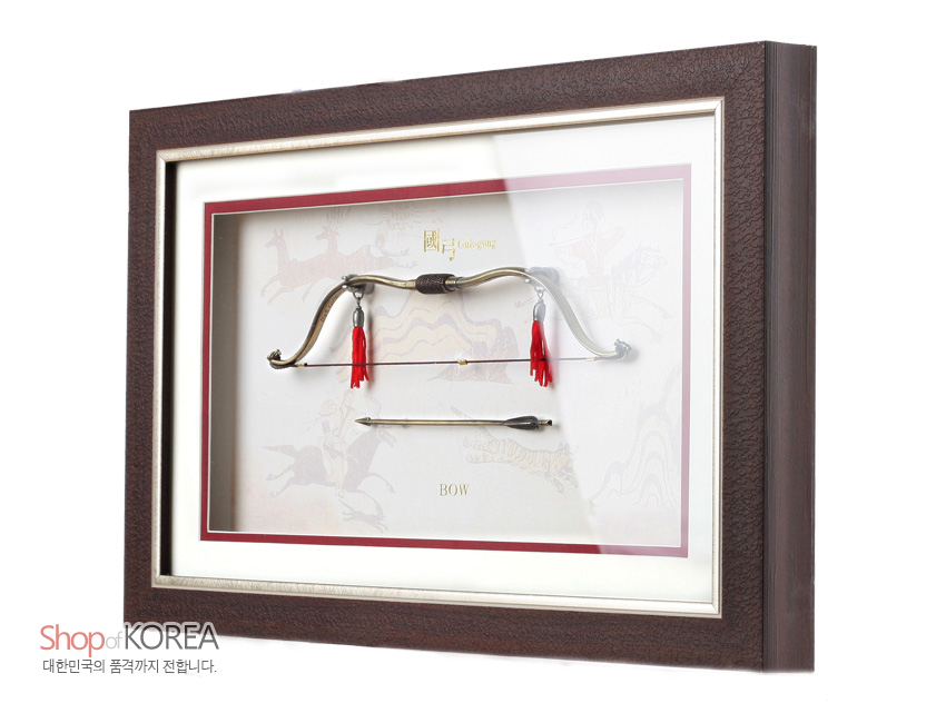 [텍스트: 國弓 Guk-gung / BOW / Shop of KOREA / 대한민국의 품격까지 전합니다.] 짙은 갈색 나무 액자 속 금속 국궁과 화살, 붉은 술 장식과 전통 수렵 문양 배경이 어우러진 입체 장식 구성