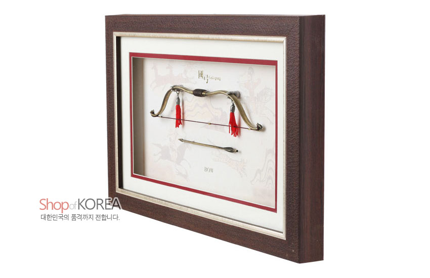 [텍스트: Shop of KOREA 대한민국의 품격까지 전합니다. 國弓 traditional bow BOW] 짙은 갈색 나무 액자 속 금속 국궁과 화살 미니어처, 붉은 술 장식과淡한 전통 수렵 문양 배경이 조화를 이룬 입체 장식 구성